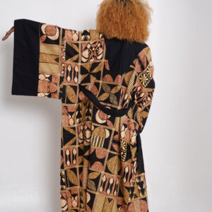 Woman wearing a long Afrincan kimono with bold tribal patterns in earthy tones, standing against a white background with one arm extended to show the wide sleeve.